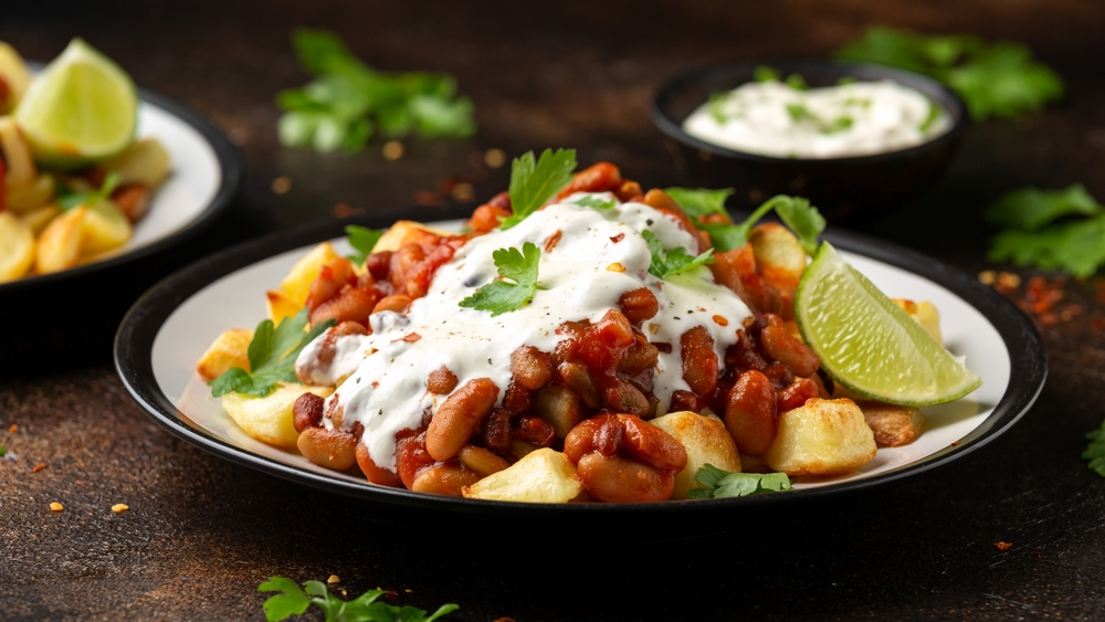 Spicy bean chili with baked potato, a staple in Mexican food, served with sour cream and lime, highlighting the use of fresh ingredients for a healthy lifestyle.