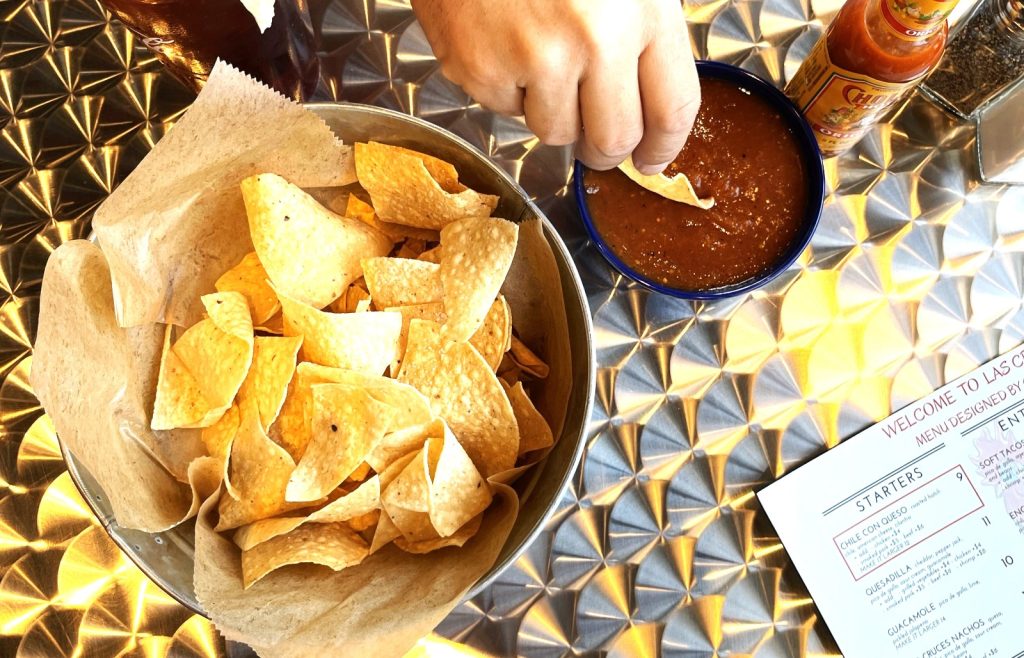 A hand dipping a chip into salsa at Las Cruces Tex Mex restaurant in Metairie, showcasing Mexican food with a basket of chips