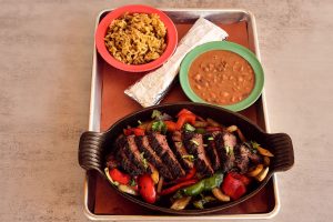 A Mexican fajita platter with steak and vegetables, with sides of rice, beans, and a tortilla, from a restaurant in Metairie, Las Cruces Tex Mex