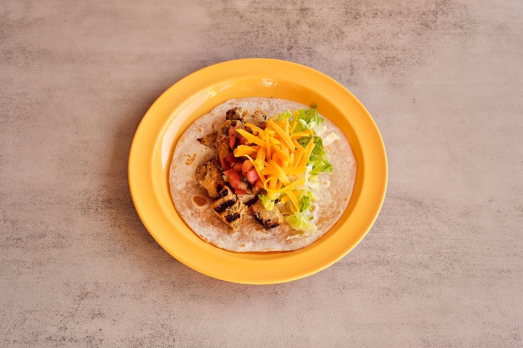 A taco with grilled chicken, diced tomatoes, shredded lettuce, and grated cheddar cheese on a soft tortilla. Mexican Food in Metairie