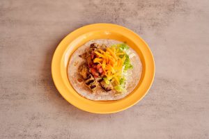 A taco with grilled chicken, diced tomatoes, shredded lettuce, and grated cheddar cheese on a soft tortilla. Mexican Food in Metairie